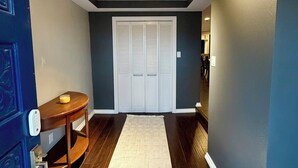 Un pasillo con suelo de madera, alfombra blanca, puerta azul con cerradura electrónica y armario blanco con puertas correderas.