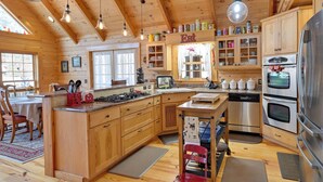 A wooden cabin kitchen with a central island, wooden cabinets, a stainless steel refrigerator, and a dining area with a table and chairs. - 1 Mi to Lake Tillery: Outdoor Retreat w/ Hot Tub! (Mt Gilead)
