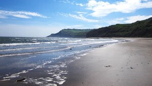 A beach with a clear sky, waves, and a distant hill. - 1 Bed in Ravenscar (oc-p30830) (Fylingdales)