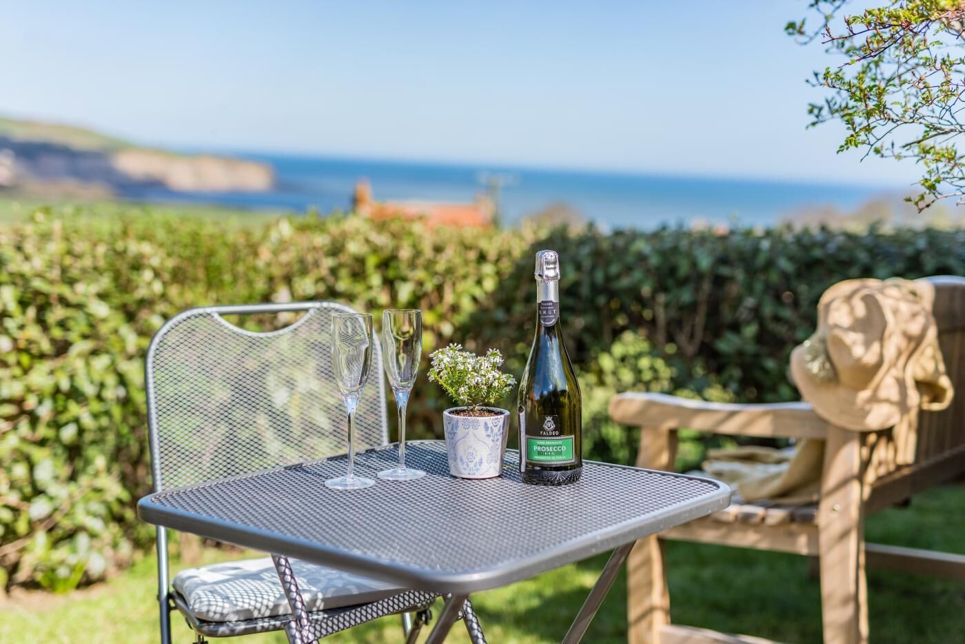 A table with a bottle of Prosecco, two glasses, and a small potted plant.