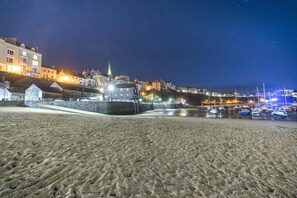 Eine Küstenstadt bei Nacht mit Sandstrand, Steinmauer und beleuchteten Gebäuden.