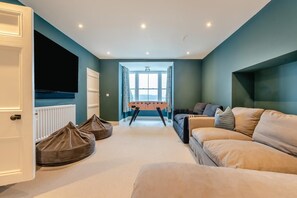 A living room with a sofa, bean bag chairs, a foosball table, and a television. - 7 Bed in Tenby (oc-b30996) (Tenby)