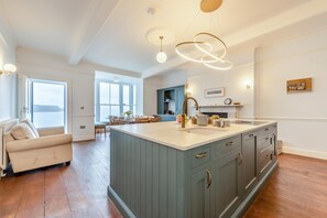 A spacious kitchen with a large island, modern pendant lights, and a view of the sea through large windows. - 7 Bed in Tenby (oc-b30996) (Tenby)