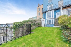 A residential area with a grassy yard, a black metal fence, and a blue house with a white window. - 7 Bed in Tenby (oc-b30996) (Tenby)