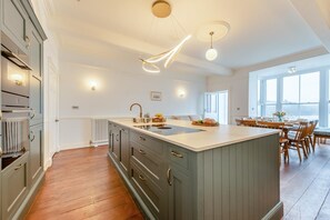 A modern kitchen with a central island, wooden cabinets, and pendant lighting. - 7 Bed in Tenby (oc-b30996) (Tenby)