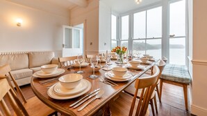 A dining room with a large table set for a meal, a sofa, and a view of the water. - 7 Bed in Tenby (oc-b30996) (Tenby)