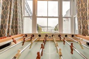A foosball table in a room with large windows and patterned curtains. - 7 Bed in Tenby (oc-b30996) (Tenby)