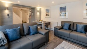 Ein modernes Wohnzimmer mit zwei grauen Ledersofas, einem Holzesstisch und einer Treppe, die zu einer oberen Etage führt.