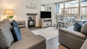 Ein modernes Wohnzimmer mit Sofa, Fernseher, Kamin und Blick auf die Terrasse.