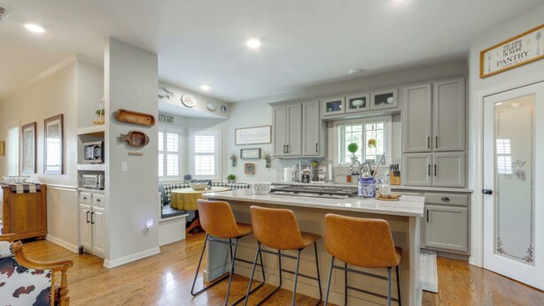 Een moderne keuken met witte kasten, een centraal eiland met barkrukken en een eethoek met een houten tafel en stoelen.