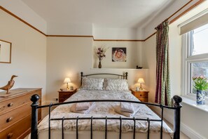 A neatly made bed with a headboard, two bedside tables with lamps, a wooden dresser, and a window with curtains. - 2 Bed in Ingleton (oc-w31066) (Ingleton)