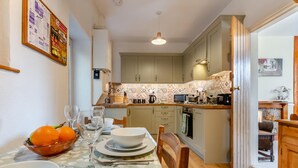 A dining area with a table set for four, a bowl of oranges, and a kitchen in the background.
