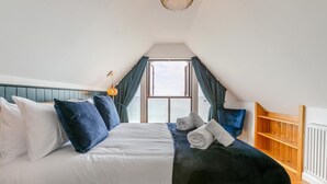 Een slaapkamer met een bed, kussens, een houten plank en uitzicht op de lucht door een raam.