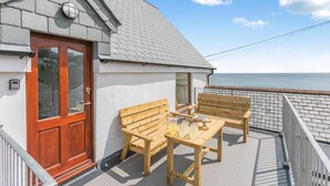 Een balkon met een houten tafel en twee houten stoelen, een rode deur en uitzicht op zee.