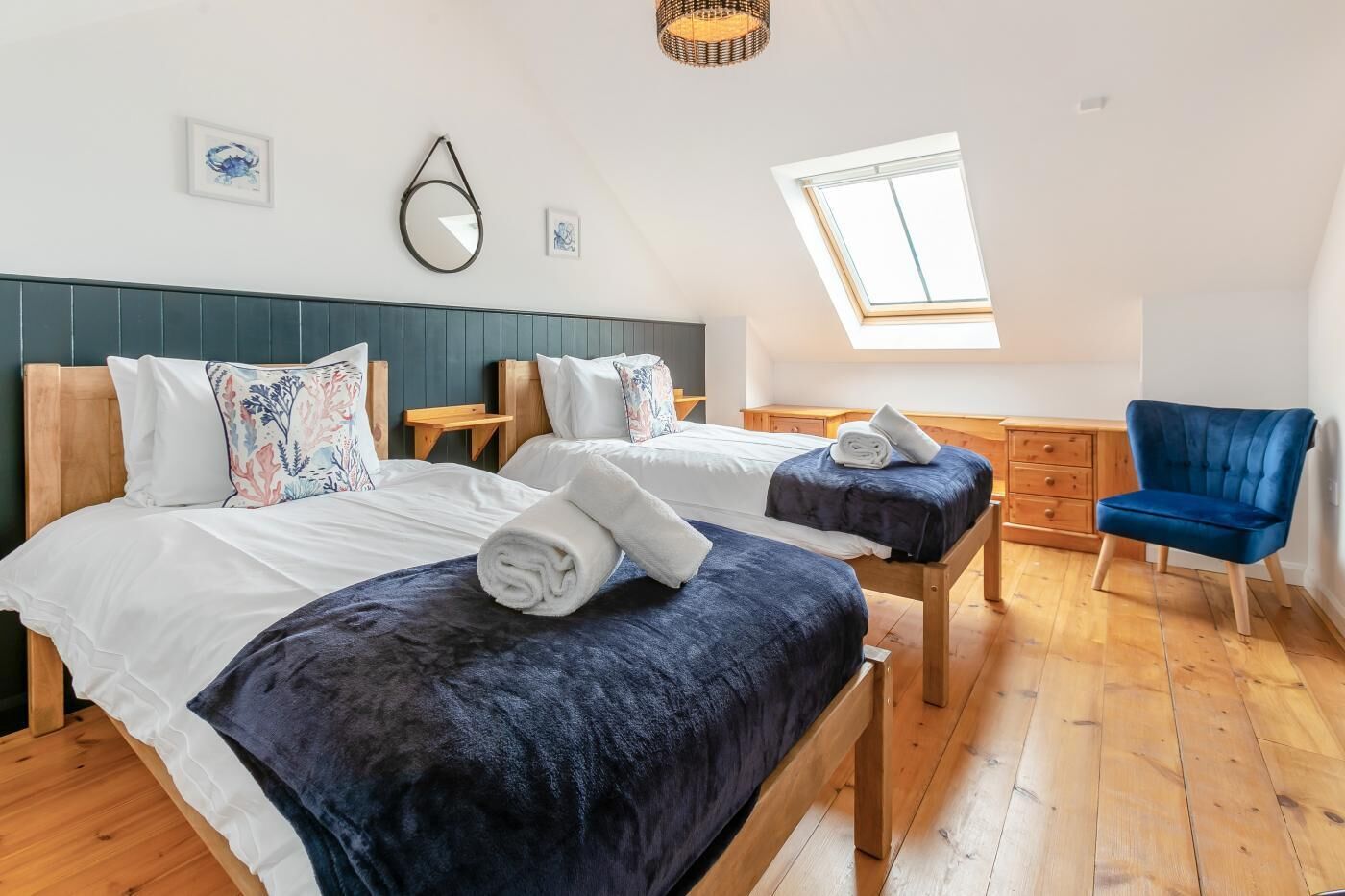 A bedroom with two beds, a blue chair, a wooden dresser, and a skylight.