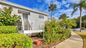 A white mobile home with a balcony, surrounded by lush greenery and palm trees.