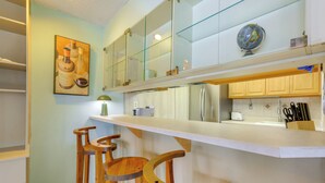 A modern kitchen with a white countertop, wooden bar stools, a stainless steel refrigerator, and a globe on the wall.