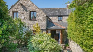 Une maison en pierre avec un toit en pente, un petit porche et un jardin où poussent différentes espèces de plantes.