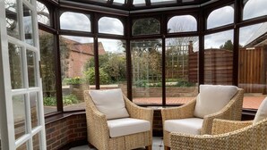 Een oranjerie met rieten stoelen en uitzicht op een tuin.