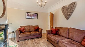 A living room with two brown leather sofas, a wooden coffee table, a fireplace, and a chandelier. - 1 Bed in Whitby (oc-l31011) (Whitby)