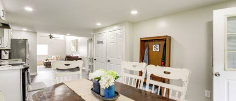 A spacious kitchen with white cabinets, a dining area with a wooden table, and a white door with a letter 'S' sign.