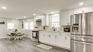 A modern kitchen with white cabinets, stainless steel appliances, and a dining area with a wooden table and chairs. - Secluded Getaway on 40 Acres in Lawrenceburg! (Lawrenceburg)