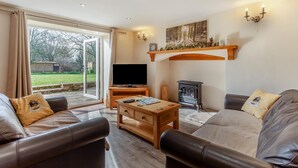 A cozy living room with a fireplace, a television, and a large window overlooking a garden. - 3 Bed in Littledean (oc-g31084) (Littledean)