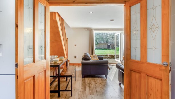 A spacious living area with a wooden staircase, a dining table with chairs, a sofa, and a sliding glass door leading to a backyard. - 3 Bed in Littledean (oc-g31084) (Littledean)