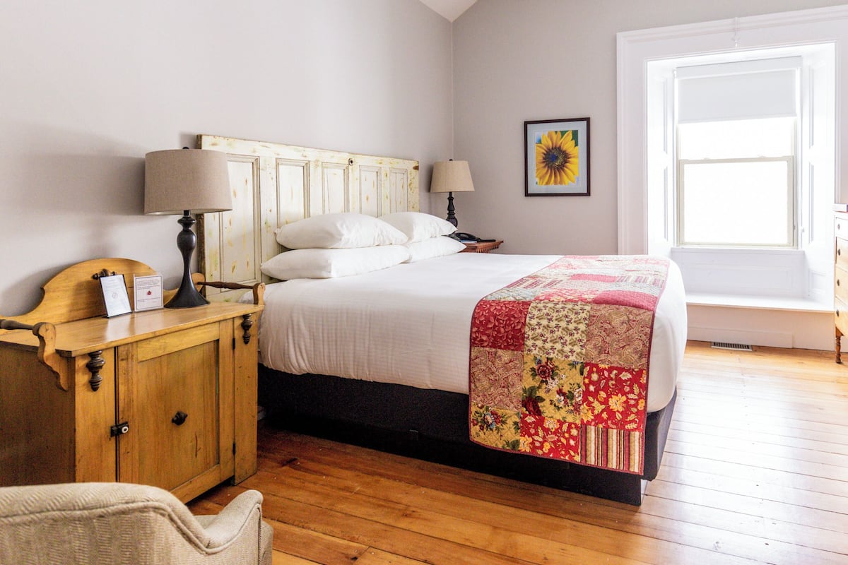 A bedroom with a wooden bed, two bedside lamps, a wooden nightstand, a chair, and a window with a view.