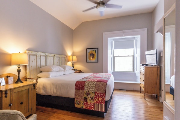 Un dormitorio con cama, lámparas de noche, cómoda de madera, ventilador de techo y ventana.