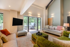 A modern living room with a sofa, ottoman, and a flat-screen TV. - 4 Bed in Ewhurst Green (oc-w31032) (Ewhurst Green)