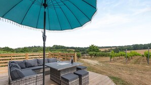 Eine Terrasse im Freien mit großem Sonnenschirm, einer Couch, einem Tisch und einem Weinglas.