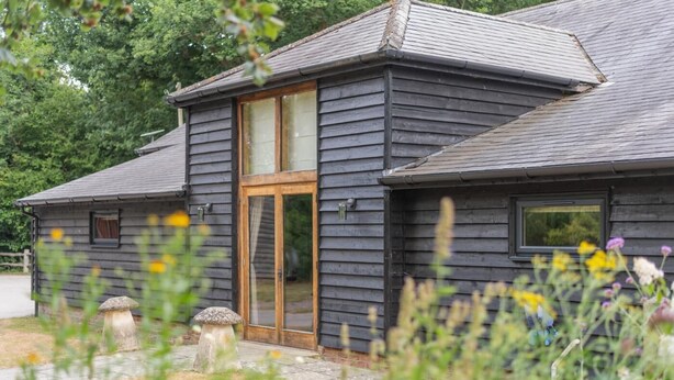 Ein zweistöckiges Holzhaus mit einem großen Glasflurtür, umgeben von einem Garten mit verschiedenen Pflanzen und Blumen.