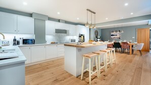 Eine moderne Küche mit weißen Schränken, einer zentralen Kochinsel mit Sitzgelegenheiten und einem Essbereich mit Tisch und Stühlen.