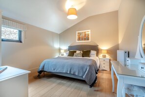 Ein Schlafzimmer mit einem Bett, Nachttischen, einer Kommode, einem Fenster mit Jalousien und einer Deckenleuchte.