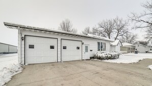 Eine Garage mit zwei weißen Türen, einer Betonauffahrt und verschneiter Landschaft.