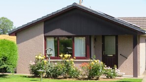 A single-story building with a dark roof and beige walls, featuring a front door, large windows, and a small porch area with a bird feeder. - 2 Bed in Insch (oc-t30986) (Newton)