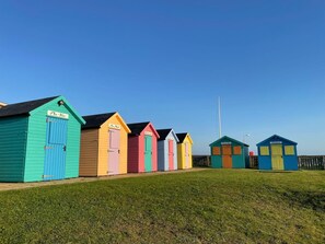 Eine Reihe bunter Strandhäuser mit einer grünen Wiese im Vordergrund und blauem Himmel.