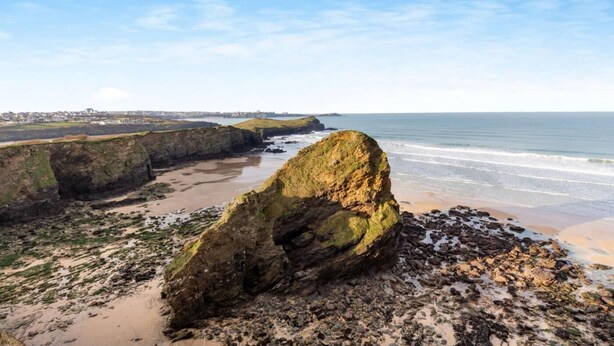 Eine Küstenlandschaft mit einer markanten Felsformation im Vordergrund, einem Sandstrand und Blick auf den Ozean.