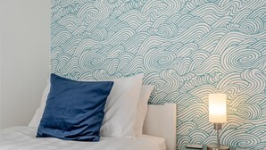 A bed with white and blue bedding, a teal bedside table with a lamp, and a wall with a wave pattern. - 2 Bed in Snettisham (oc-d31668) (Snettisham)