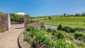 A patio area with a brick wall, a table, and a chair, overlooking a green landscape with a river. - 2 Bed in Seaford (oc-l31115) (Seaford)