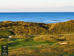 Ein Golfplatz mit Fahnenstange, Sandbunkern und Blick auf das Meer.