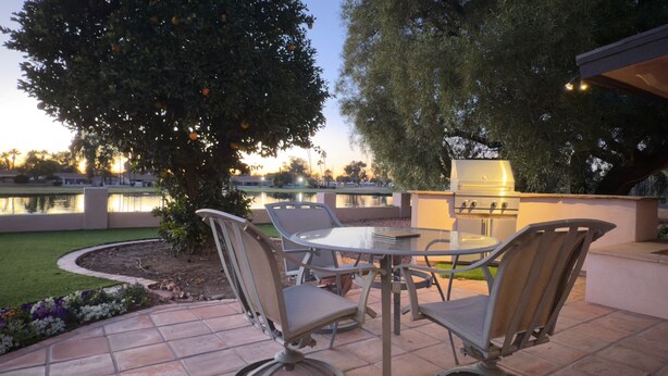An outdoor patio with a table and chairs, a grill, and a view of a body of water. - Desert Oasis backing Golden Hills Golf Course. (Mesa)