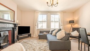 A modern living room with a fireplace, a sofa, a TV, and a chandelier. - 2 Bed in Swanage (oc-b31105) (Swanage)