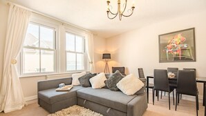 A modern living room with a grey sectional sofa, fluffy white rug, and a dining area with black chairs and a table. - 2 Bed in Swanage (oc-b31105) (Swanage)