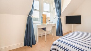 A bedroom with a bed, a desk, a chair, a TV, and a window with curtains. - 2 Bed in Swanage (oc-b31105) (Swanage)