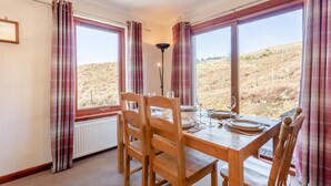En spiseplads med et bord til fire, store vinduer med gardiner og udsigt over et tørt landskab.