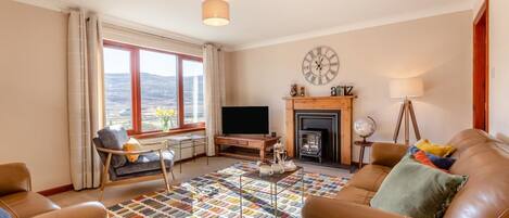 A living room with a fireplace, a sofa, a television, and a view of the outdoors.