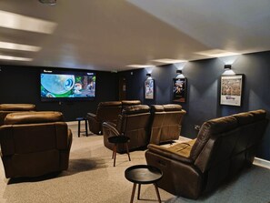 Ein Heimkinozimmer mit Ledersesseln, einem großen Flachbildfernseher und gerahmten Filmplakaten an der Wand.