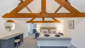 Een slaapkamer met een groot bed, een kaptafel, een spiegel en een plafond met zichtbare houten balken.